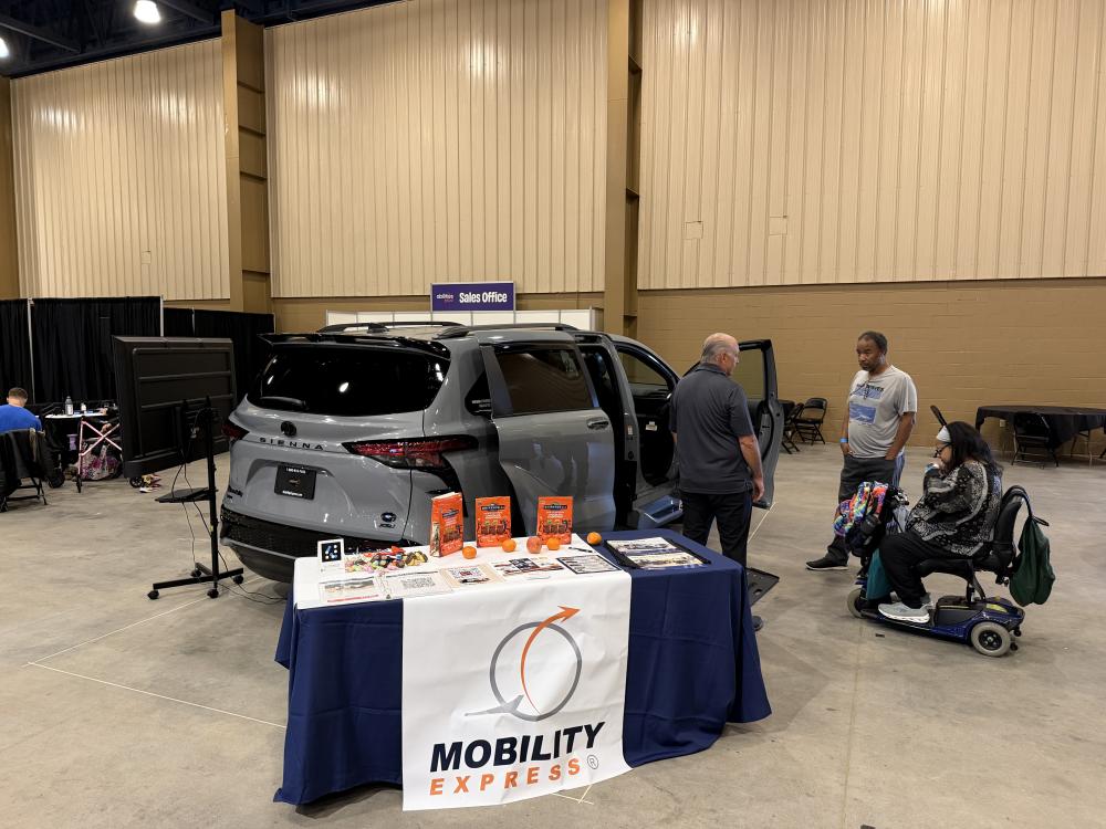 A wheelchair van specialist shows a man and woman (the woman in a wheelchair) a 2026 Toyota Sienna wheelchair van at the Mobility Express booth at Abilities Expo Orlando 2026.