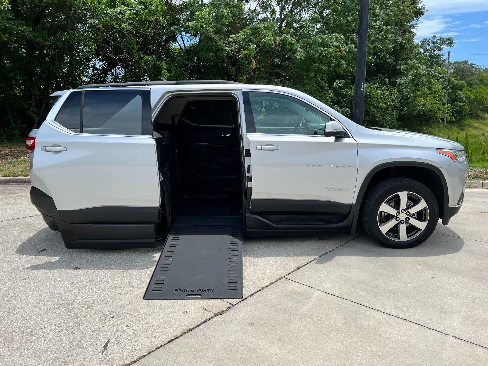 Silver Chevrolet Traverse wheelchair accessible suv with ramp deployed from open passenger side rear door.