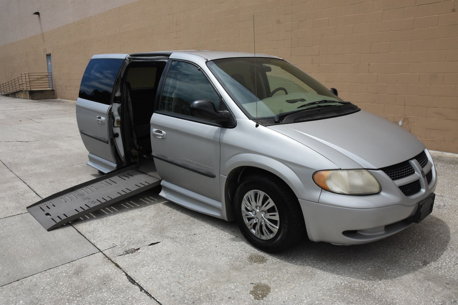 Passenger side of a silver 2003 Dodge Grand Caravan Wheelchair Van, with ramp deployed, as seen from front angle