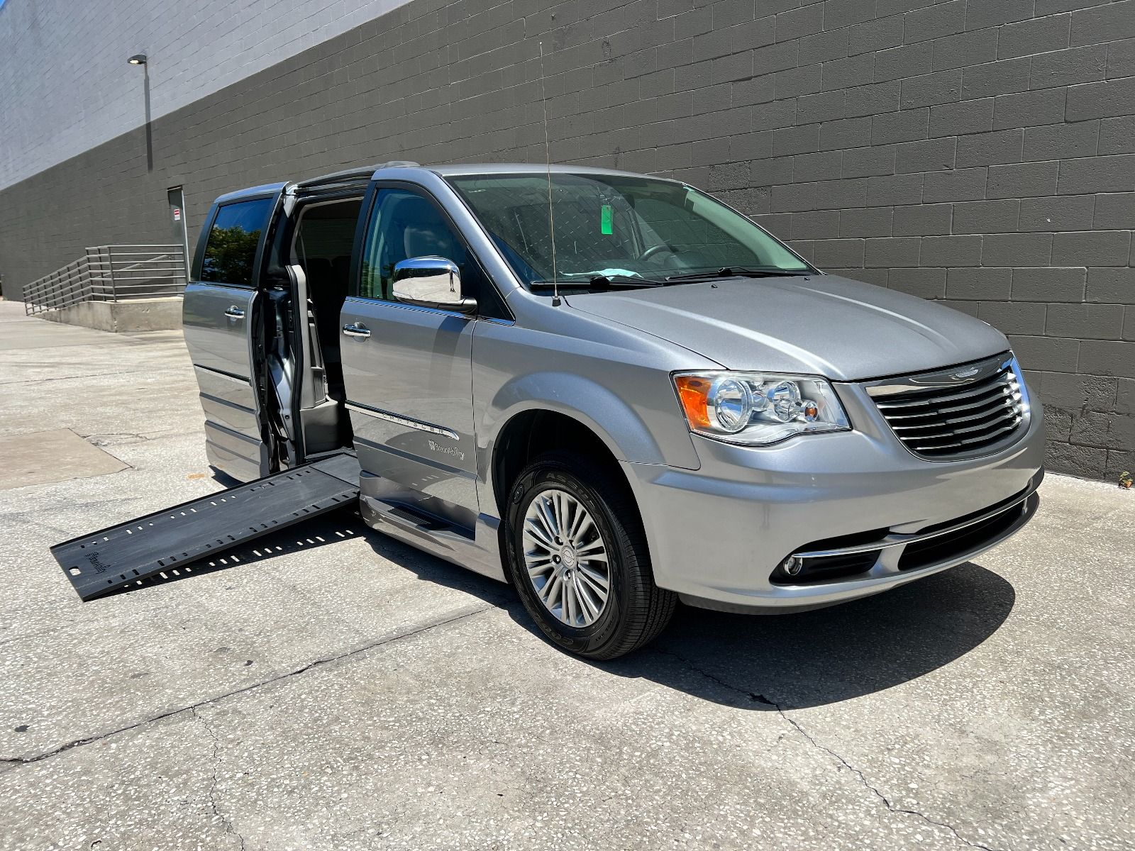 Silver 2016 Chrysler Town & Country wheelchair van with ramp deployed from passenger sliding door, as seen from front passenger angle.