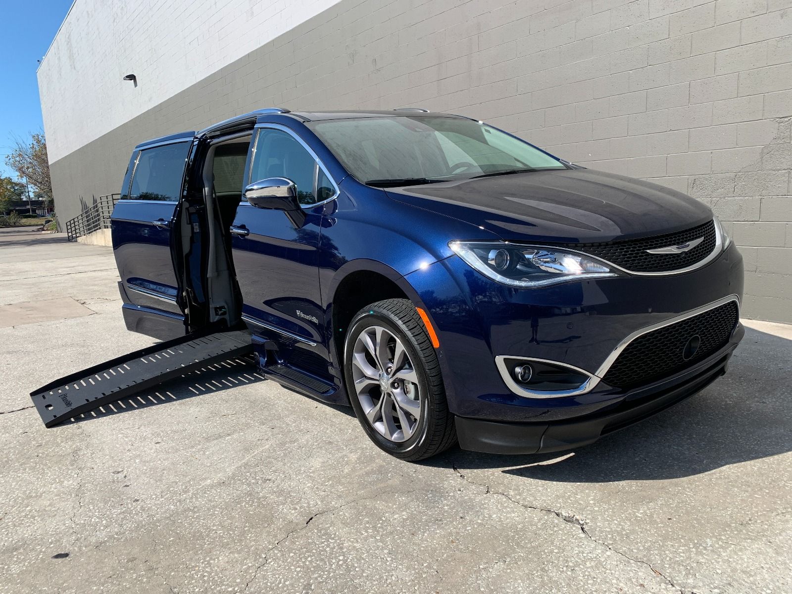 Blue 2020 Chrysler Pacifica wheelchair van with ramp deployed from passenger sliding door, as seen from front passenger angle.