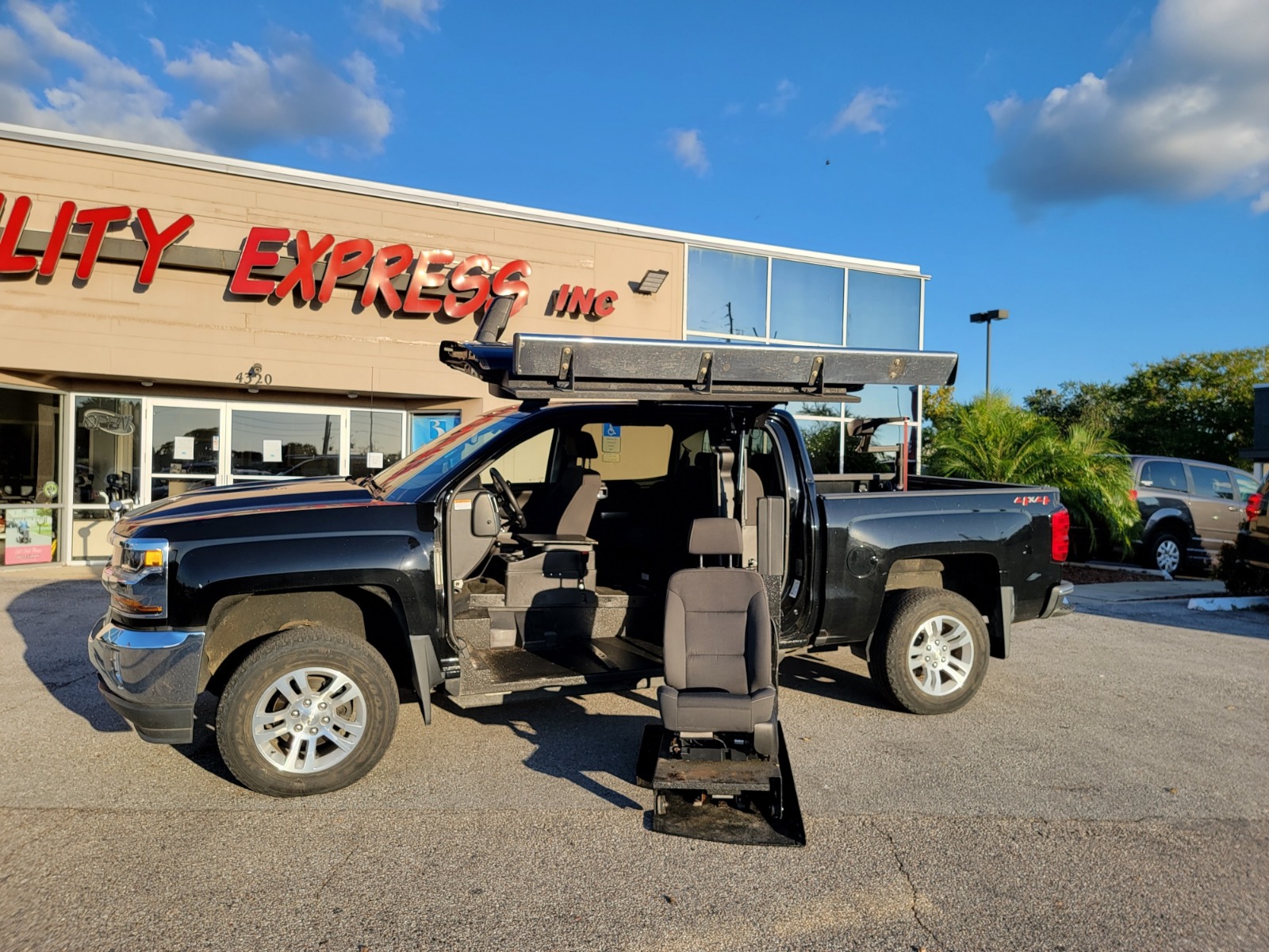 Black Chevrolet Suburban wheelchair accessible suv with lift deployed from open passenger side front door.