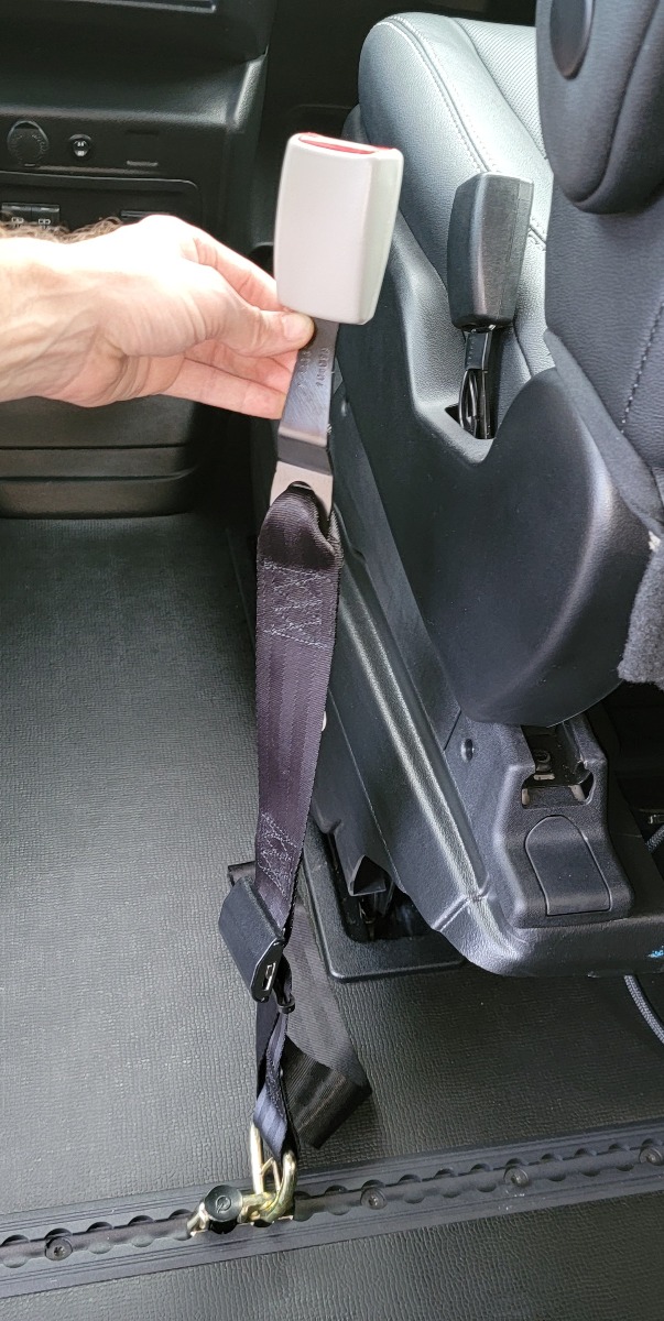 Standard L-Track seat belt adapter being held up.