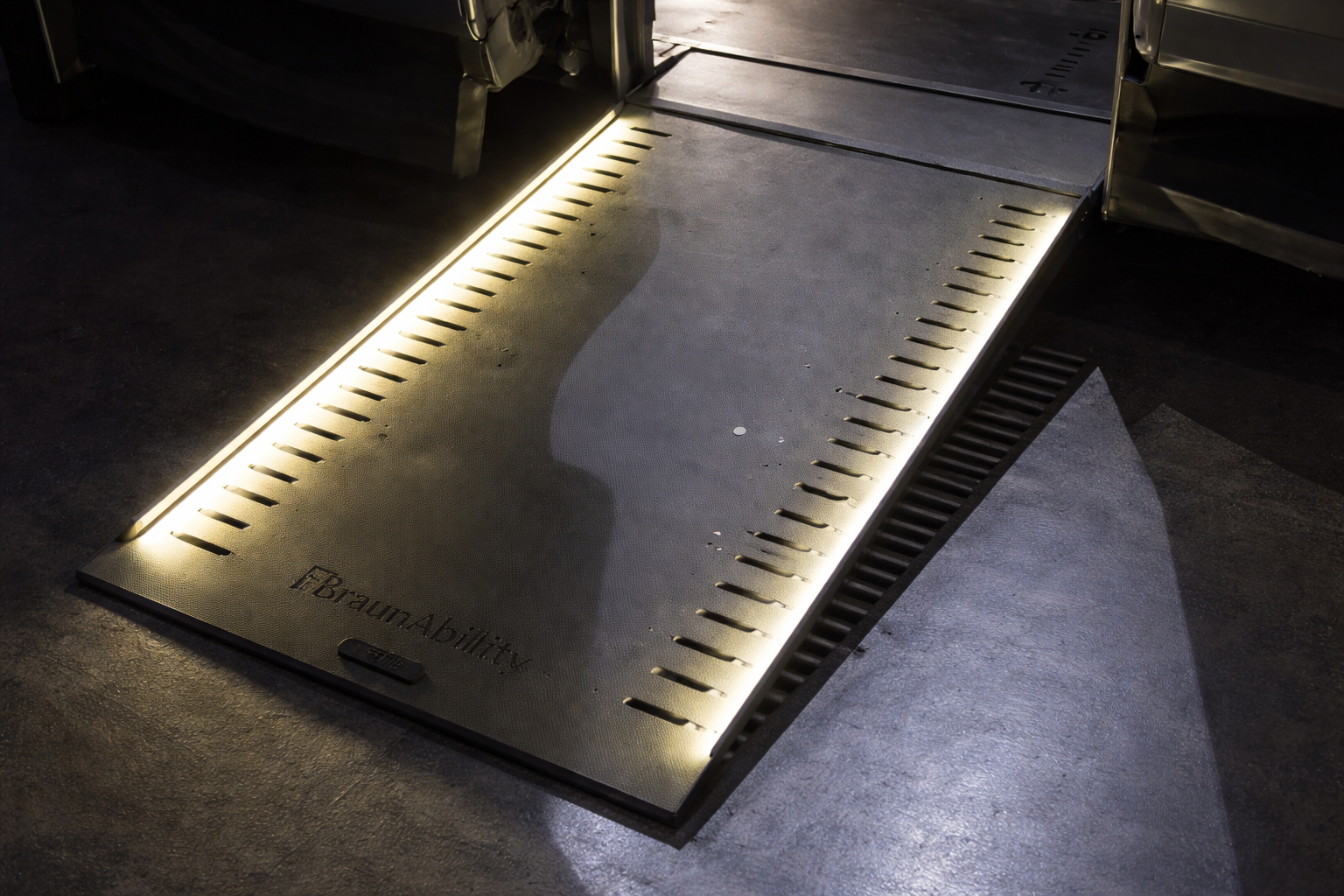 A black aluminum ramp with led light strips lining either edge, being deployed from a wheelchair accessible Chevrolet Traverse. Only the ramp is completely visible.