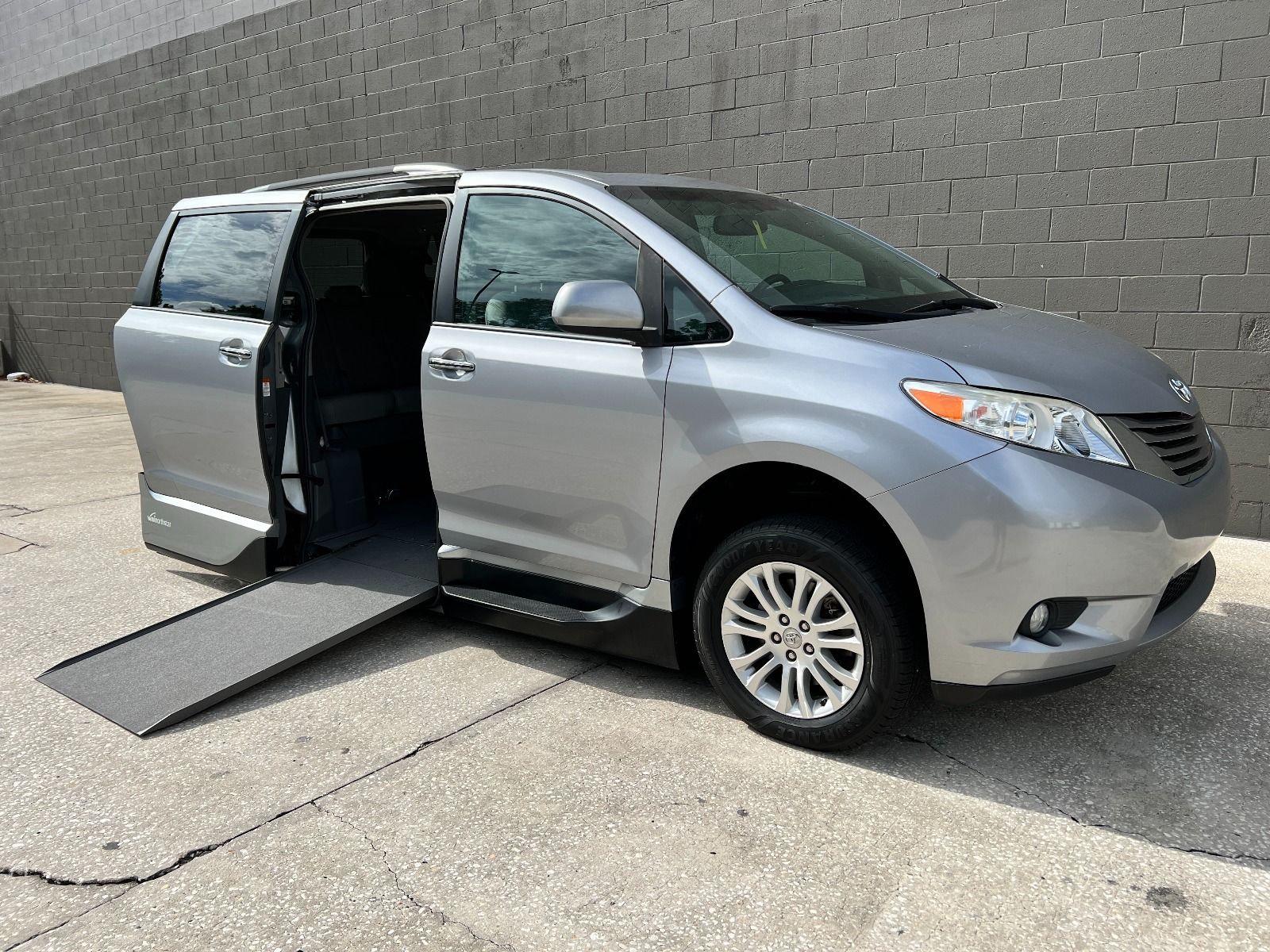 Silver Toyota Sienna wheelchair van with sliding door open and ramp deployed, viewed from front corner angle.