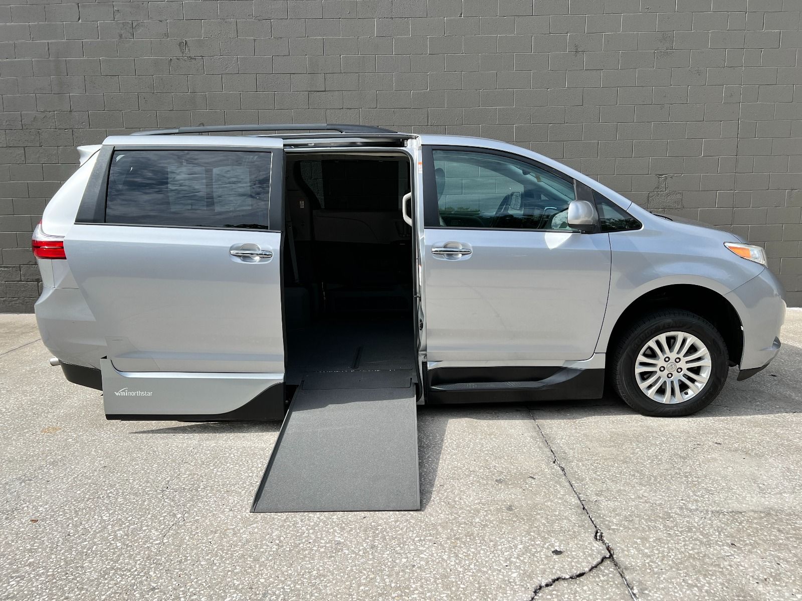 Silver Toyota Sienna wheelchair van with sliding door open and ramp deployed.