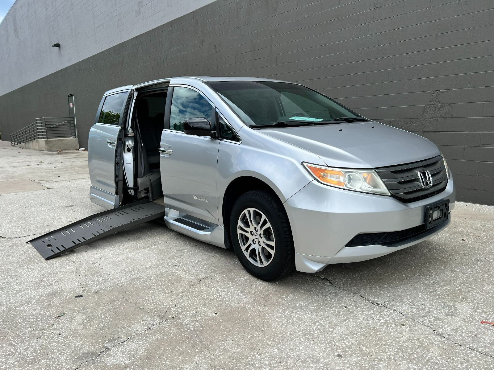 Passenger side of a silver 2012 Honda Odyssey Wheelchair Van, with ramp deployed, viewed from front angle