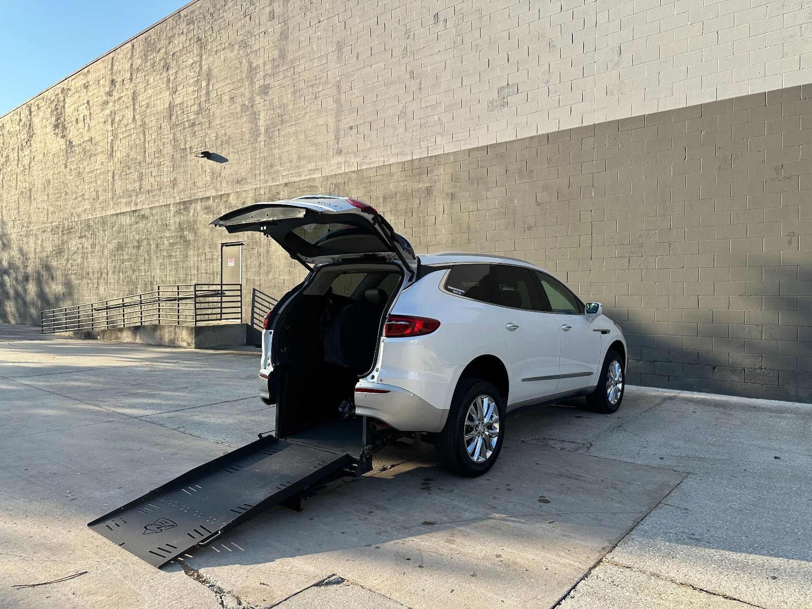 White Buick Enclave SUV rear entry wheelchair accessible SUV conversione ramp deployed from open rear hatch.