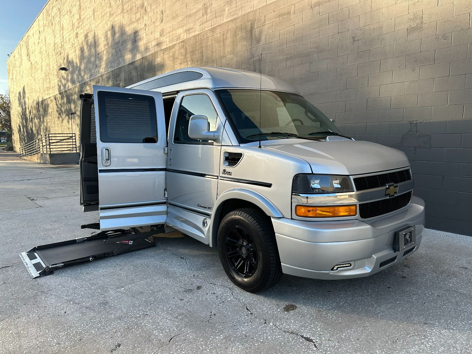 Chevrolet Express Full Size Wheelchair Van with lift system deployed from passenger side barn style doors, as seen from front angle.