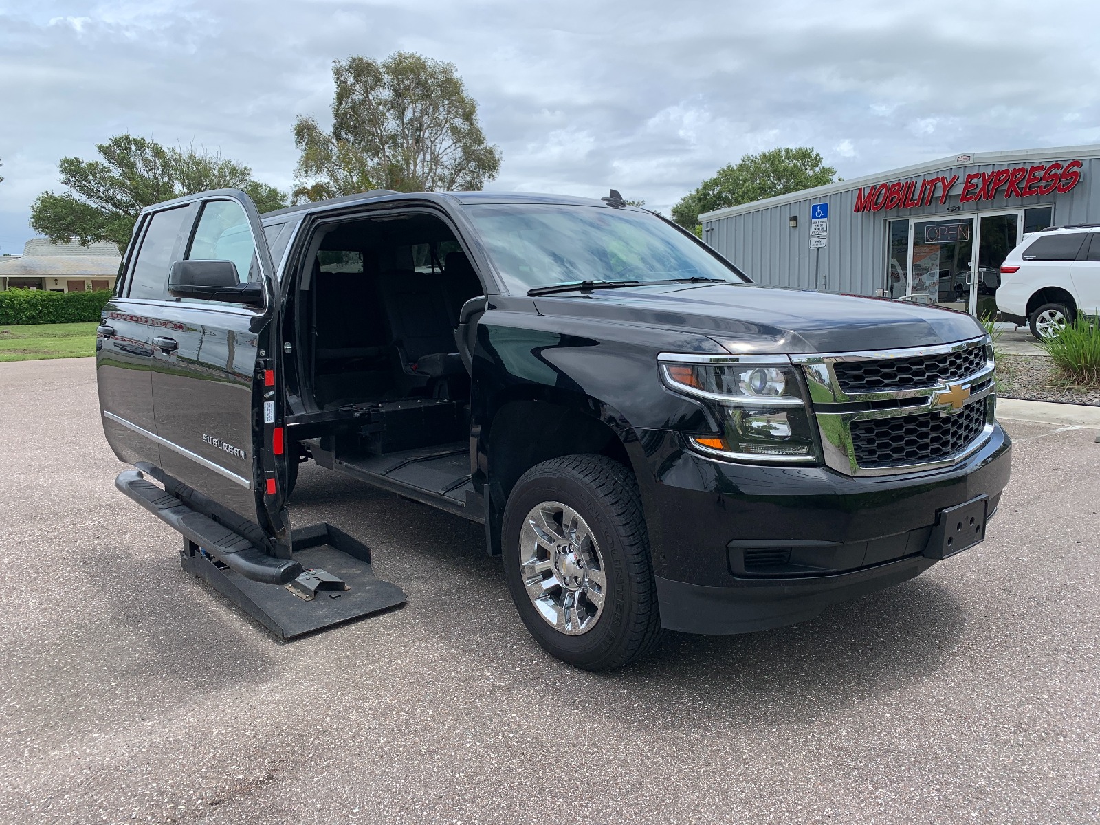 Black Chevrolet Suburban wheelchair accessible suv with lift deployed from open passenger side front door.