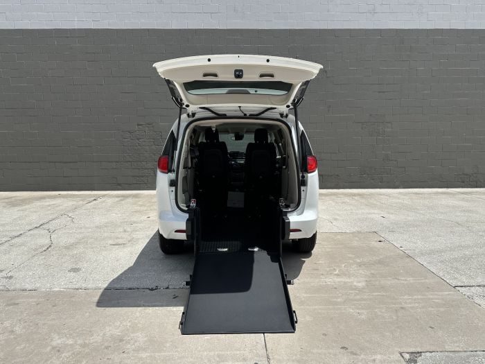 White Chrysler Pacifica with rear entry wheelchair van conversion with ramp deployed from open rear hatch.