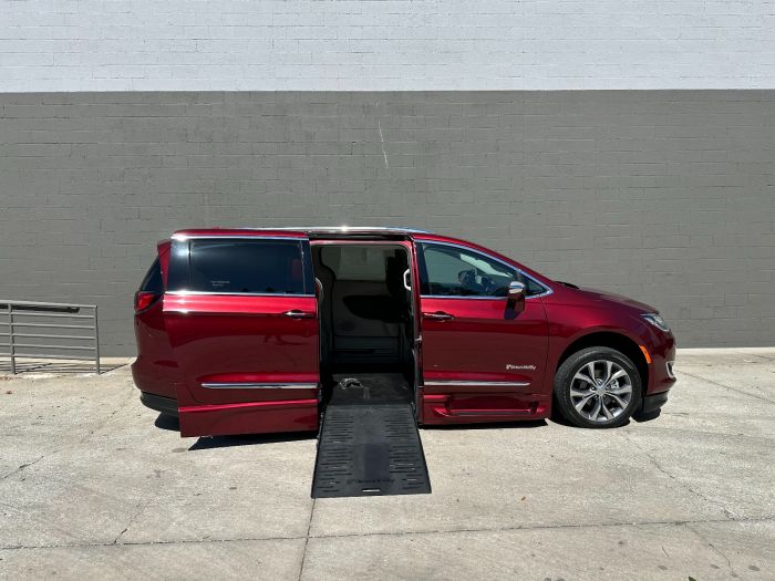 Red Chrysler Pacifica wheelchair van with the ramp deployed from the open passenger side sliding door.