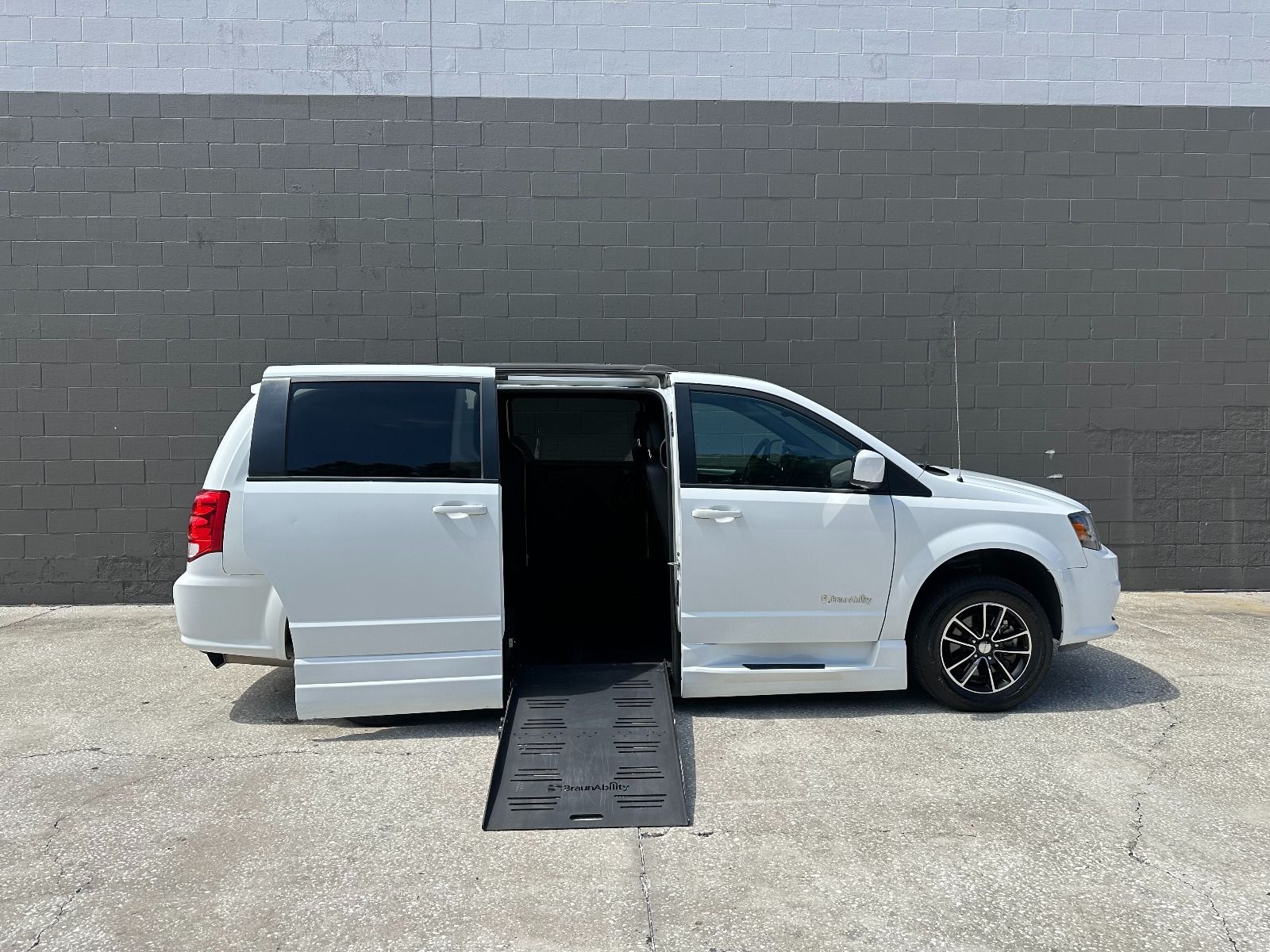 White Dodge Grand Caravan wheelchair van with the ramp deployed from the open passenger side sliding door.