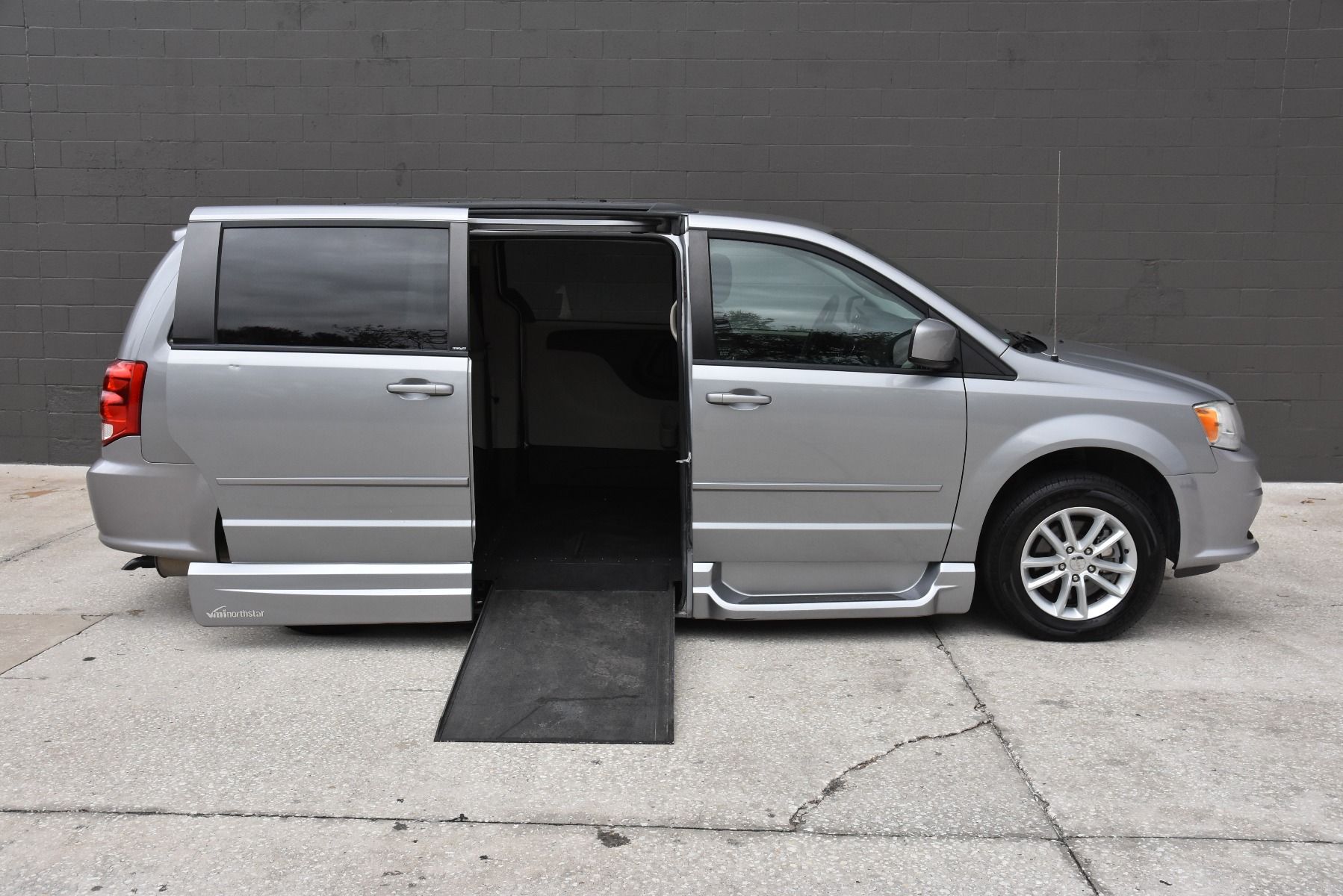 Silver Dodge Grand Caravan with in floor ramp wheelchair van conversion deployed from open passenger sliding door.