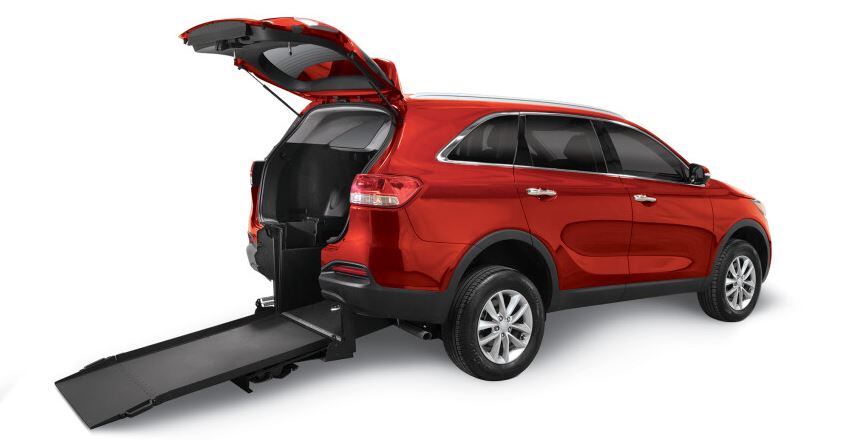 A red wheelchair accessible Kia Sorento with a rear entry wheelchair access conversion with the rear hatch open and the ramp deployed.