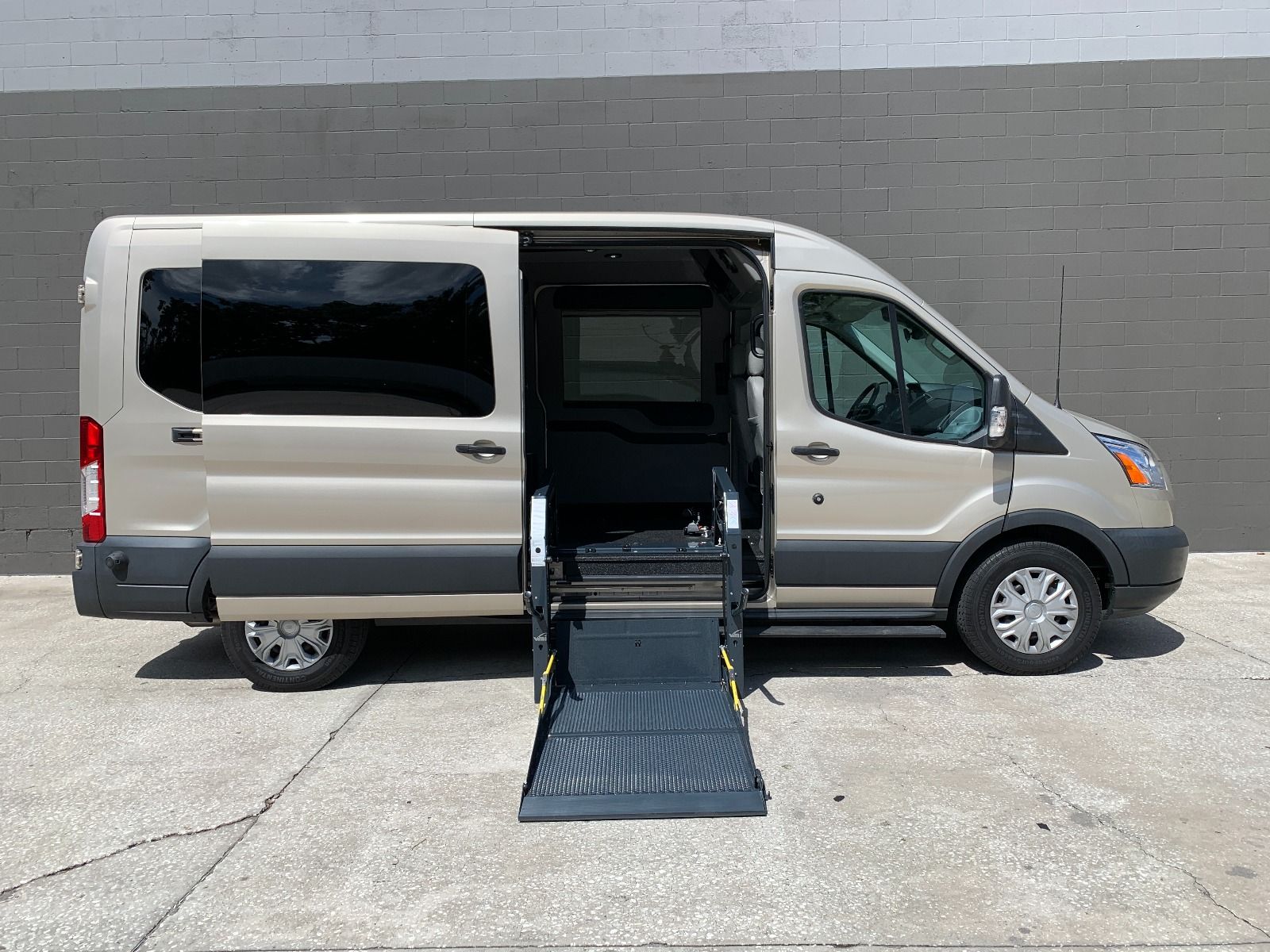 Passenger side of a gold 2017 Ford Transit Full Size Wheelchair Van, with lift deployed