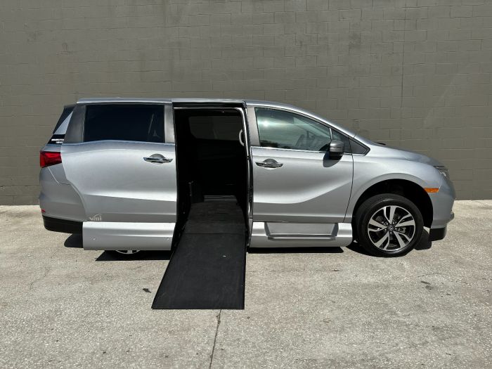 Silver Honda Odyssey wheelchair van with sliding door open and ramp deployed from passenger sliding door.