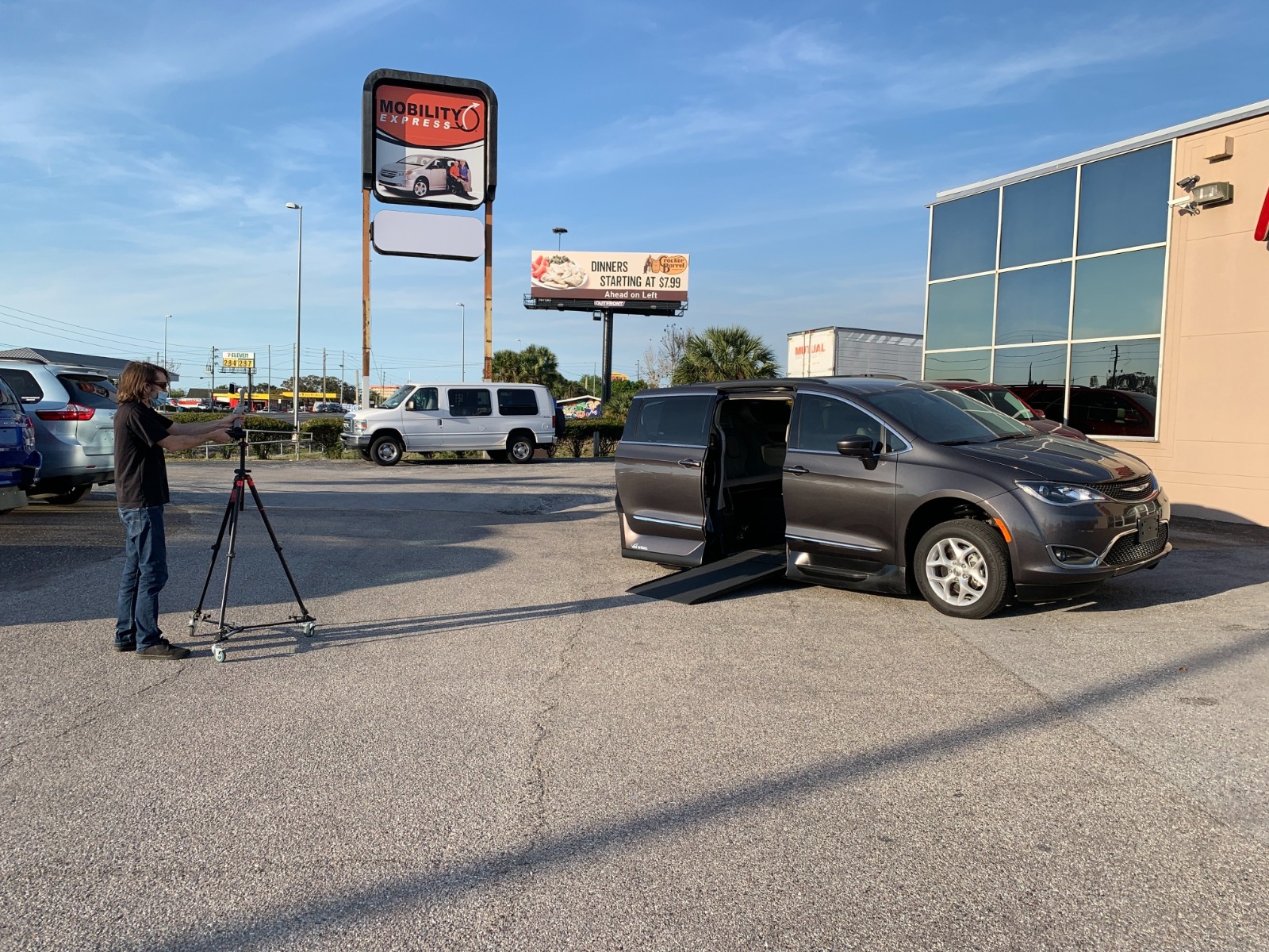 Man standing with a camera tripod looking at a van.