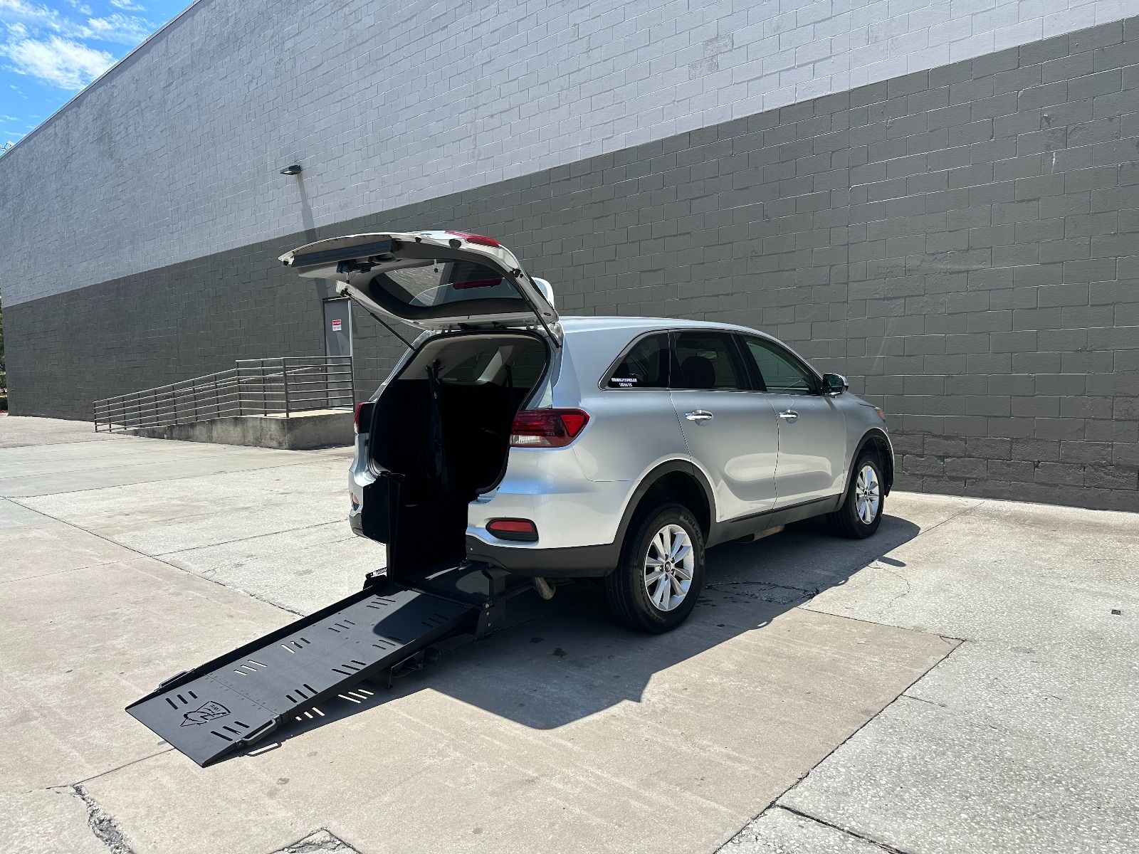 Silver Kia Sorento wheelchair accessible SUV with rear entry conversion with ramp deployed from open rear hatch.