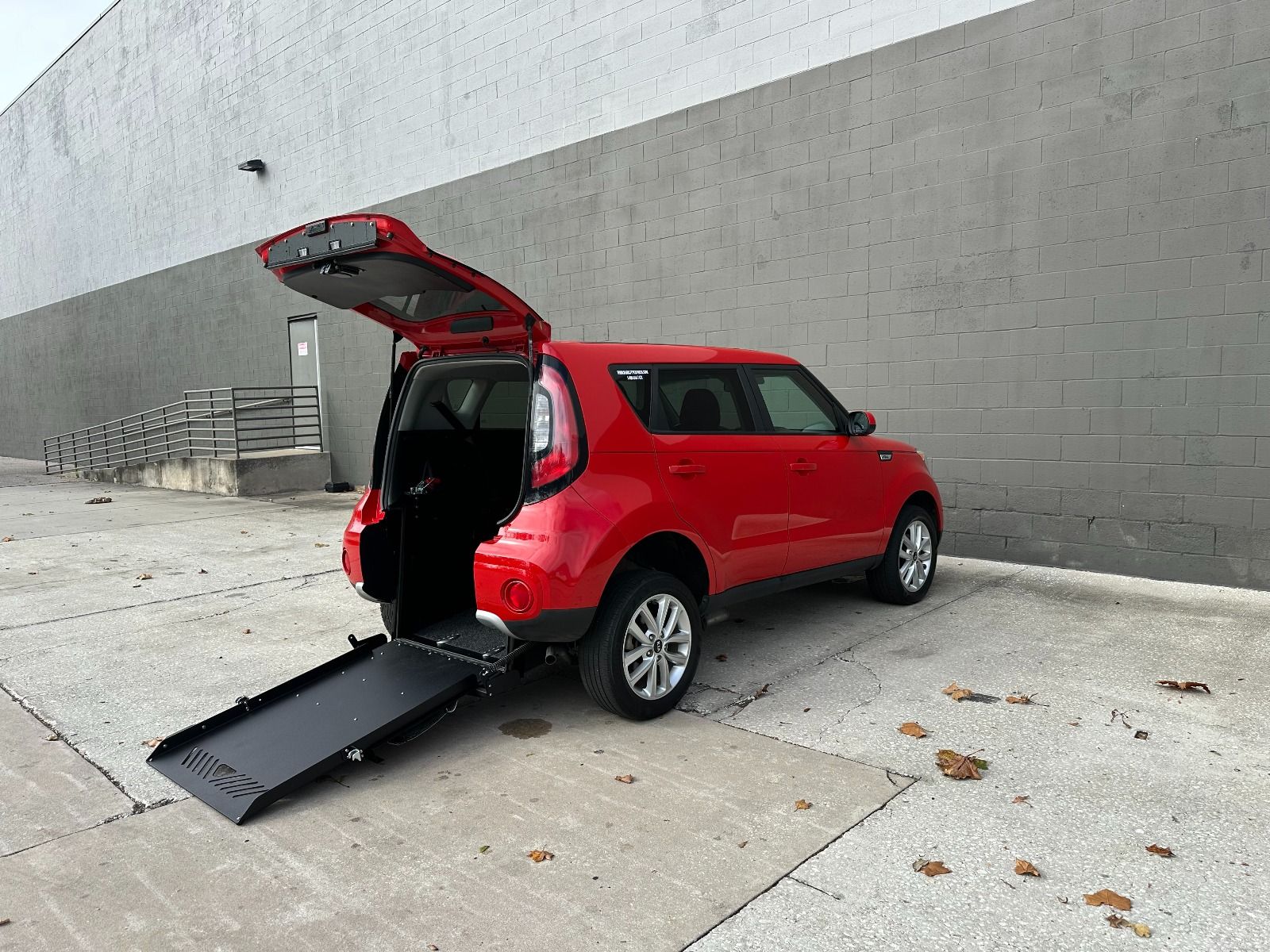 Red Kia Soul wheelchair accessible SUV with rear entry conversion with ramp deployed from open rear hatch.