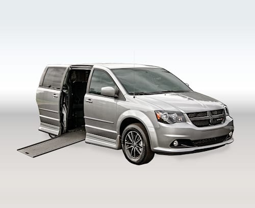 A silver Dodge Grand Caravan with Rollx side entry conversion with ramp deployed from open passenger sliding door.