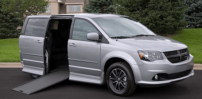 A silver Dodge Grand Caravan with a Rollx wheelchair van conversion with ramp deployed from open passenger sliding doorway.