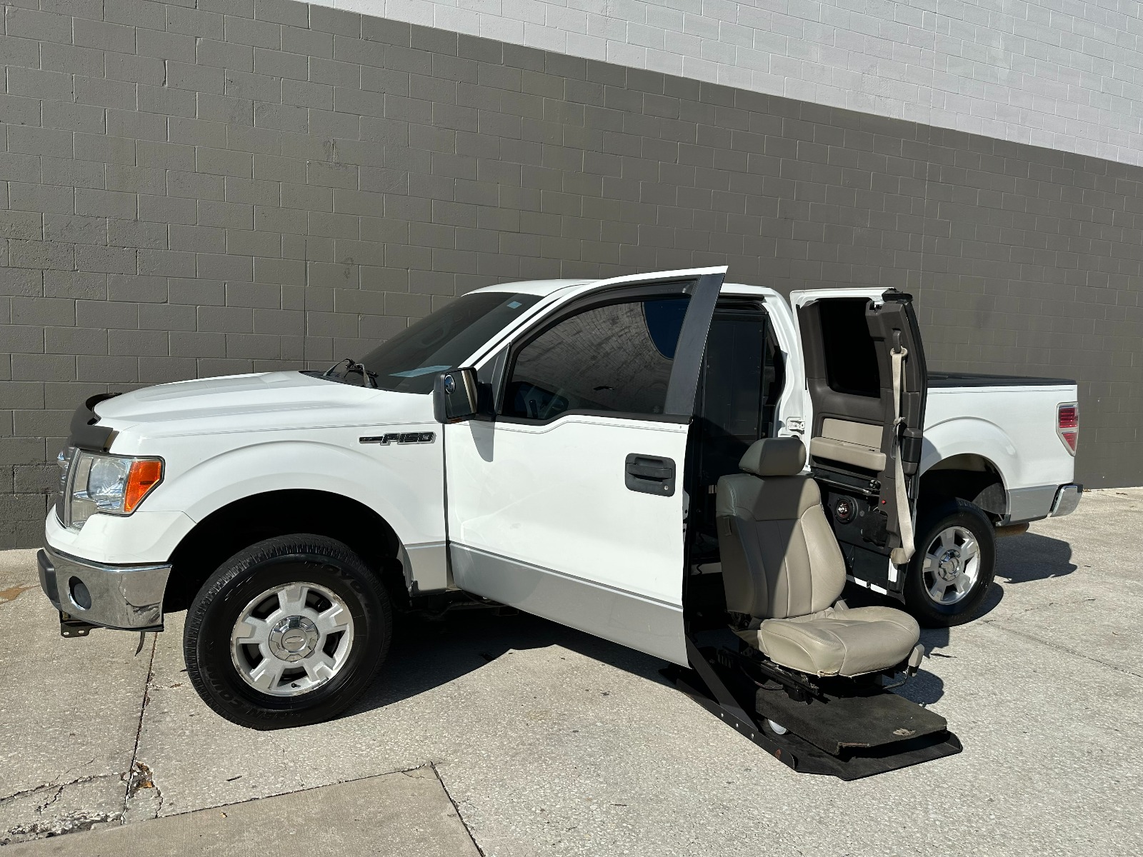 White Ford F-150 Wheelchair Accessible Truck with lift deployed from open driver side doors.